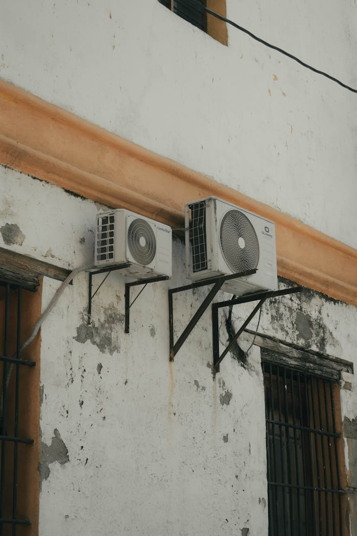 services-02 Two outdoor AC units installed on a weathered concrete wall for cooling purposes.